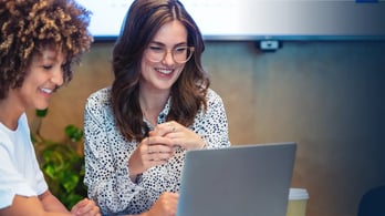 two happy female hr managers looking at their computer to assess gift card program 