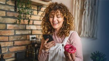 female gift card recipient looking at phone while eating donut