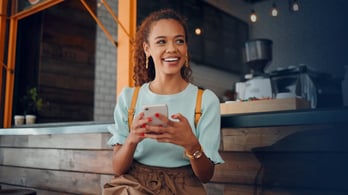 happy female customers sitting on a stool in a coffee shop, and using her phone 