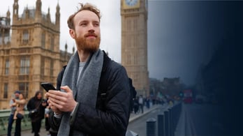 man with a smartphone in his hands looking to the side against the backdrop of Big Ben Tower