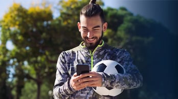soccer player getting a gift card on his phone while holding a soccer ball and smiling