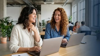two happy employees sitting togehter on their laptops during a strategy session