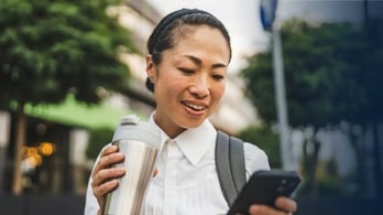 woman drinking coffee in a thermos she got from a gift card on her phone that she's looking at