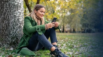 woman sitting under a tree happy to be getting a digital reward on her phone